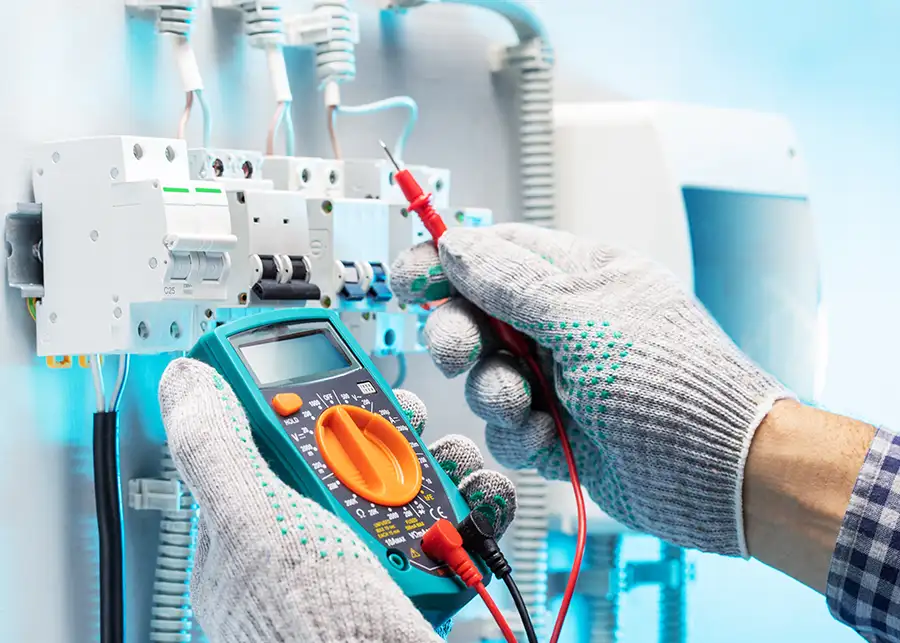Gloved electrician using a digital multimeter to test circuit breakers in an electrical panel — JSE Service and Electric LLC, O'Fallon, IL and St. Louis, MO