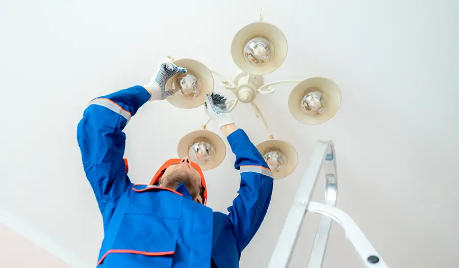 Electrician on a ladder installing a multi-bulb ceiling light fixture — JSE Service and Electric LLC light fixture installation in O'Fallon, IL and St. Louis, MO