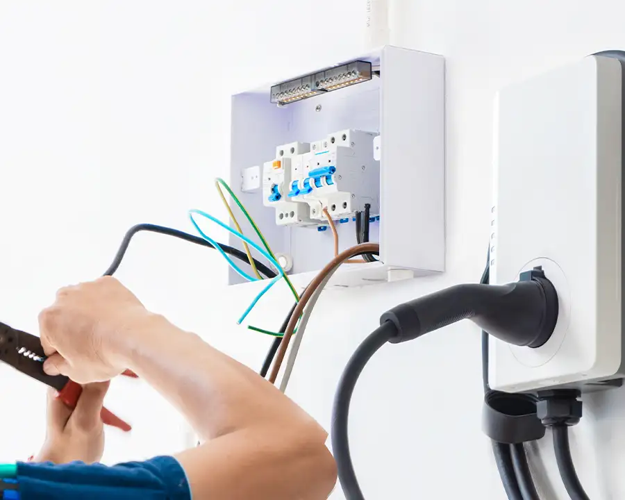 Close-up of an electrician connecting wiring to a dedicated circuit breaker panel next to a mounted EV charging unit — JSE Service and Electric LLC EV charger installation in O'Fallon, IL and St. Louis, MO