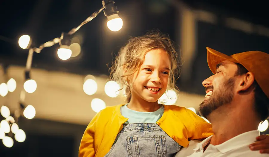Father and daughter laughing together under warm outdoor string lights — JSE Service and Electric LLC outdoor and landscape lighting installation in O'Fallon, IL and St. Louis, MO