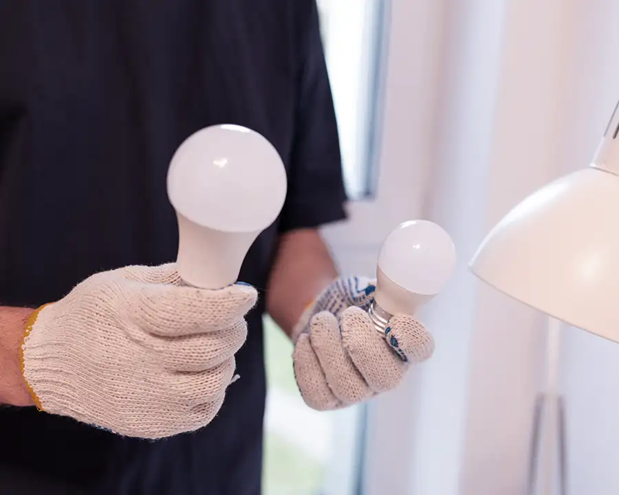Gloved electrician holding two LED light bulbs for comparison during a lighting upgrade — JSE Service and Electric LLC energy-efficient LED lighting services in O'Fallon, IL and St. Louis, MO