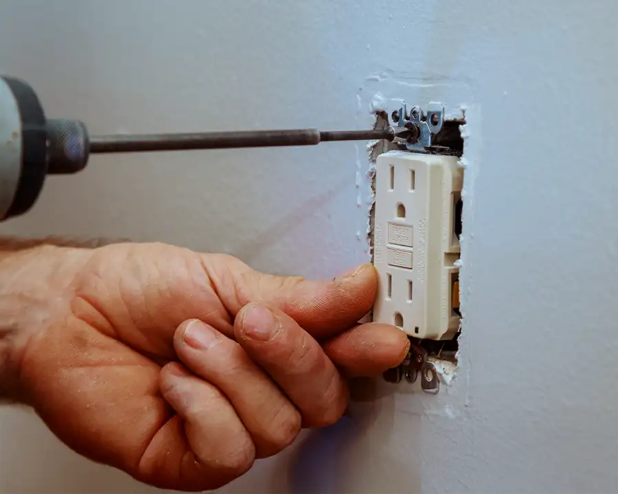 Electrician using a screwdriver to install a GFCI outlet in a wall — JSE Service and Electric LLC outlet installation and replacement in O'Fallon, IL and St. Louis, MO