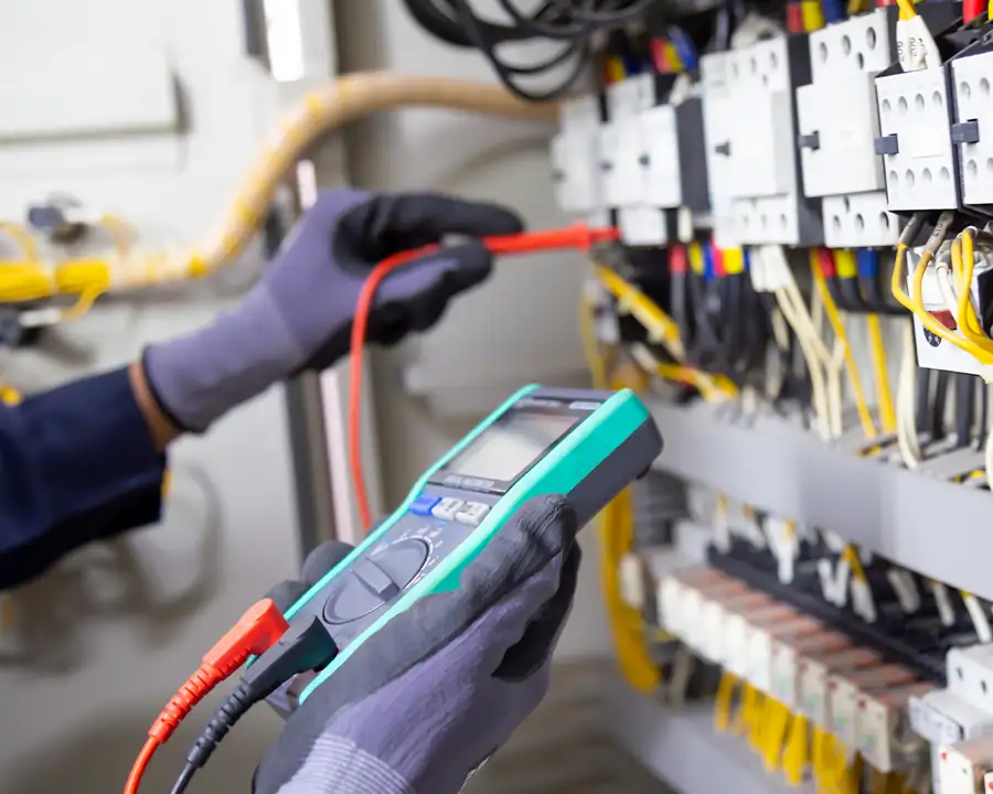 JSE Service and Electric LLC technician uses a digital multimeter to test an electrical control panel for a commercial building — serving O'Fallon, IL and St. Louis, MO