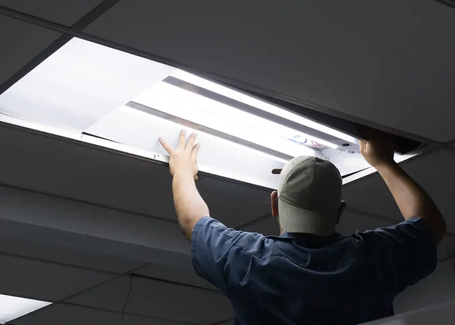 JSE Service and Electric LLC technician seating a fluorescent troffer into a suspended grid ceiling during a commercial lighting retrofit in Troy, IL